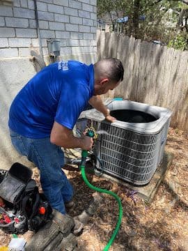 Technician flushing and cleaning an outdoor air conditioning condenser coil