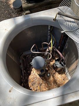 Inside an AC condensing unit before cleaning, showing debris around the compressor