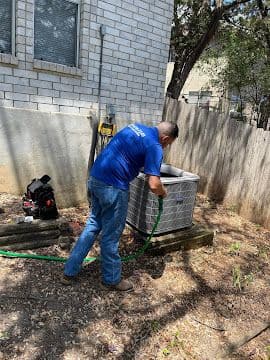 Technician rinsing condenser coils during a summer AC maintenance visit