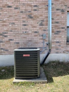Goodman air conditioning condenser installed on a concrete pad against brick