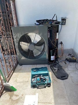 Heat pump condenser being serviced with tools laid out on the patio